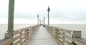 Long wooden pier over cloudy ocean view.