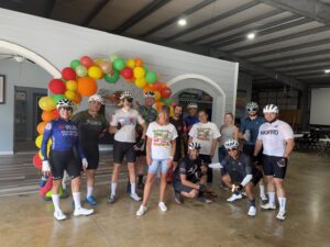 Cyclists posing under colorful balloon arch.